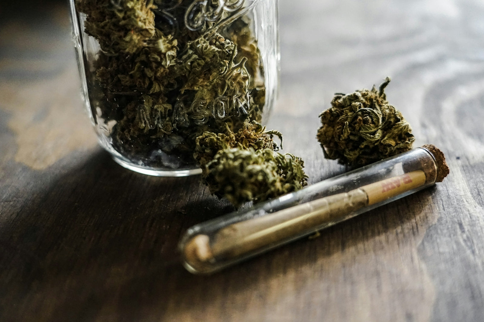 a glass jar filled with marijuana sitting on top of a wooden table